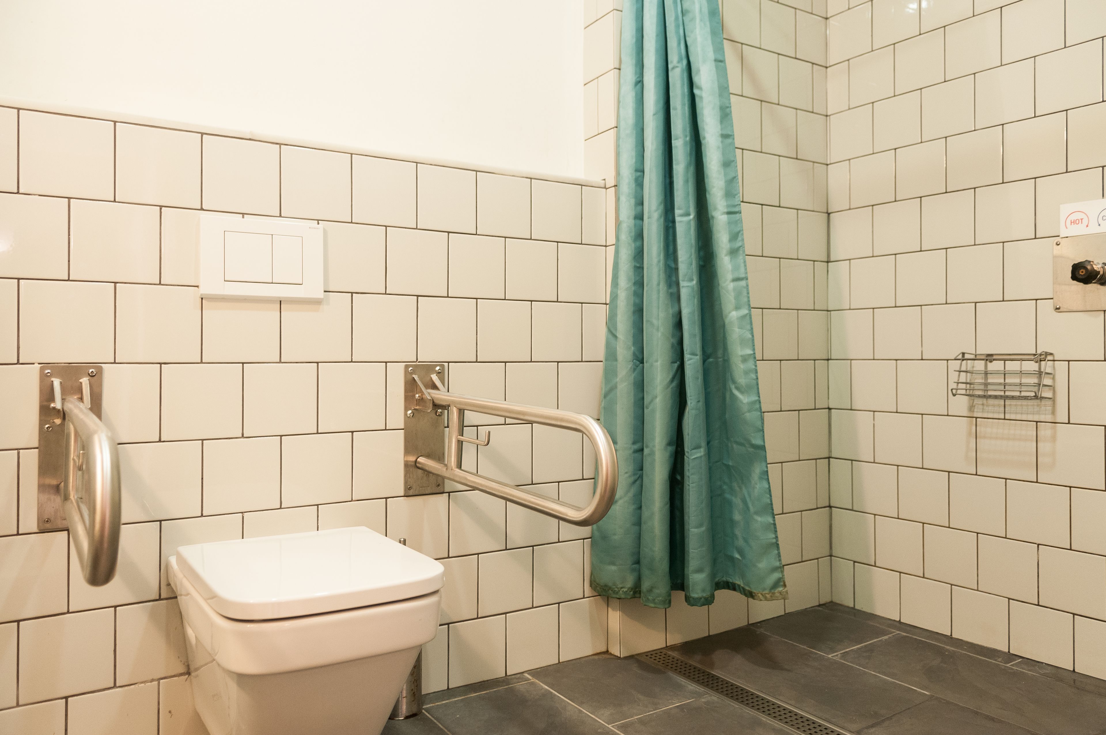 Een badkamer met witte tegels, een wit toilet, een handgreep, een blauwgroen douchegordijn en een handdroger.