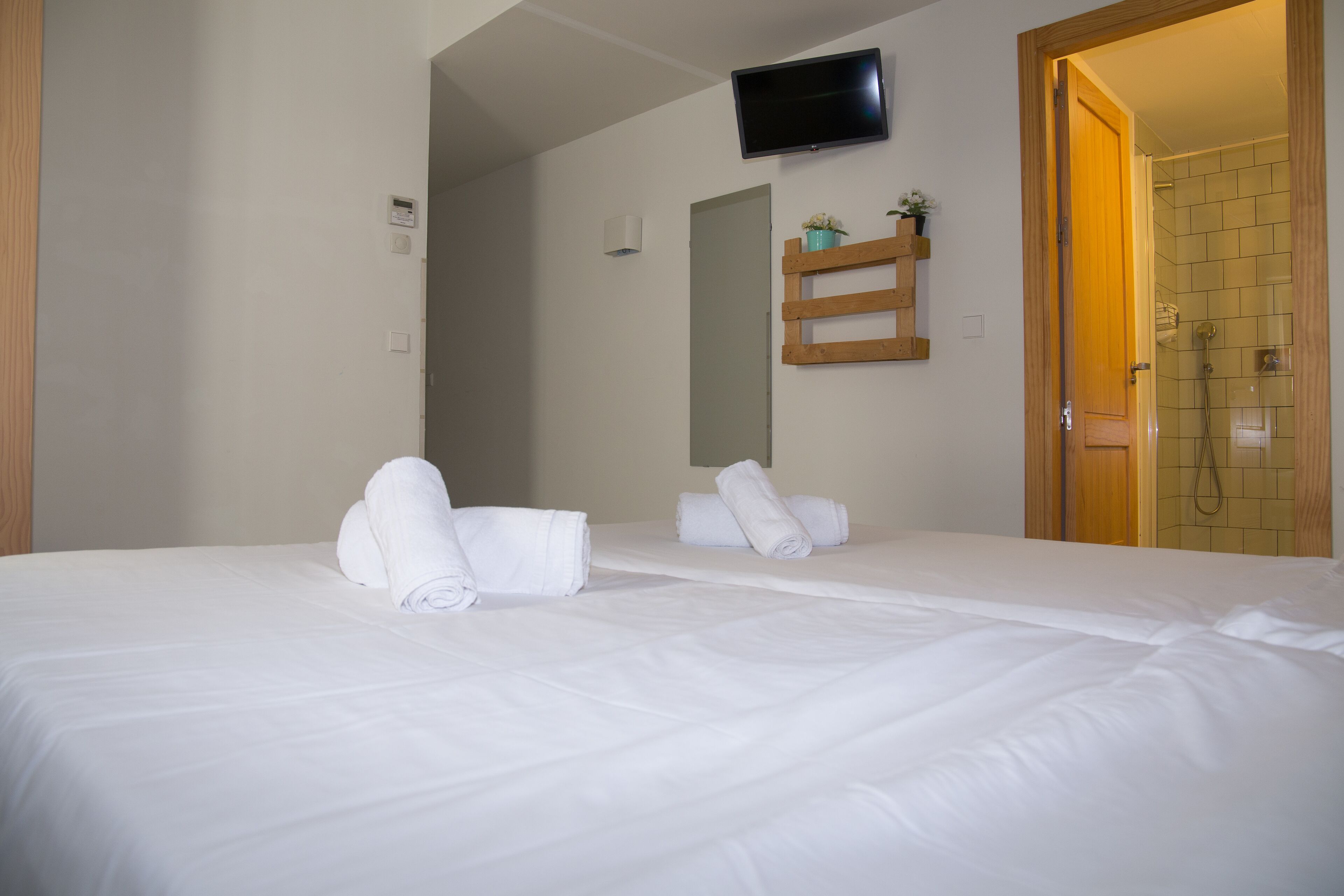 A hotel room with a bed, a TV mounted on the wall, and a shower area visible through an open door.
