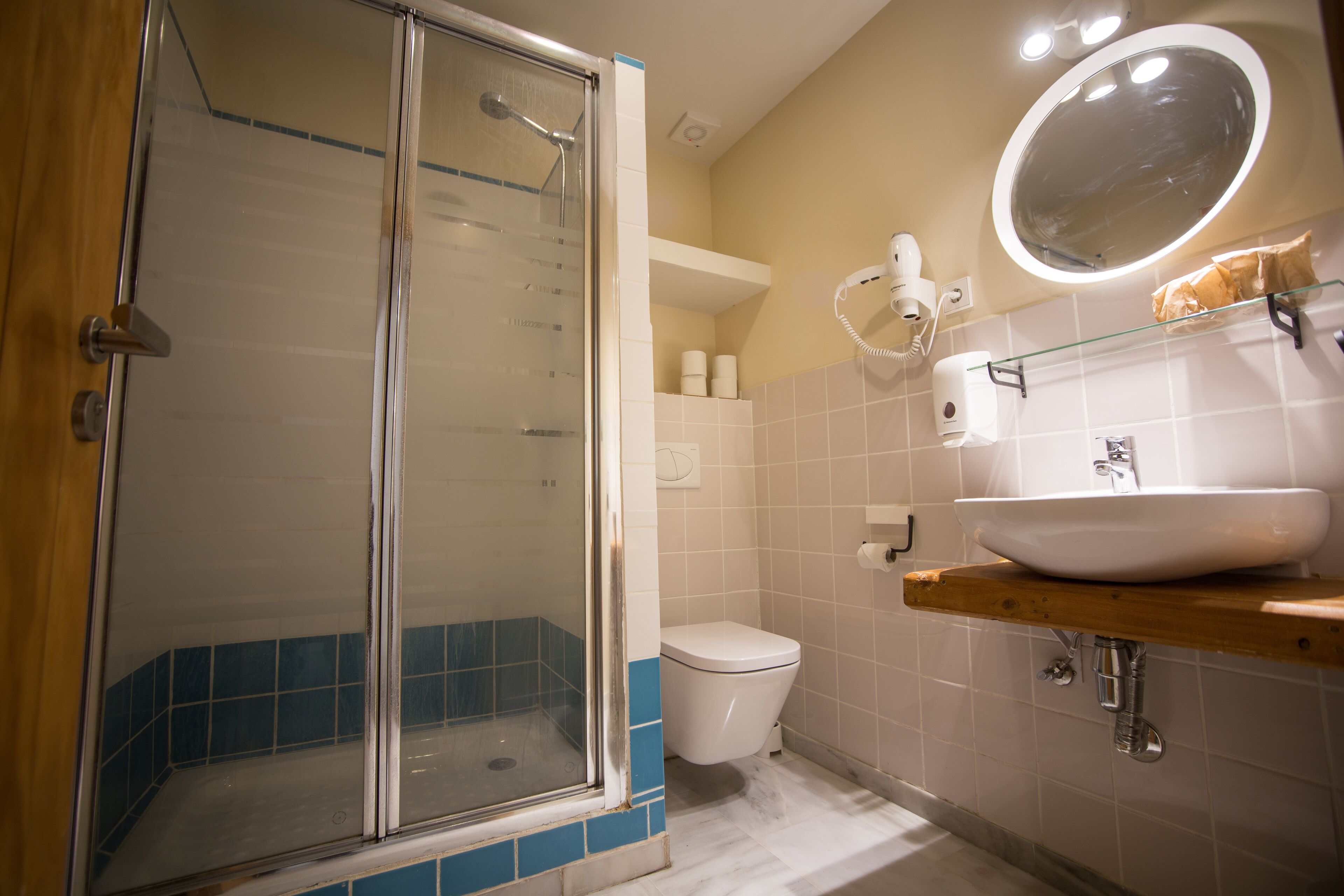 A bathroom with a glass-enclosed shower, a white toilet, a sink with a mirror above it, and a shelf with toiletries.