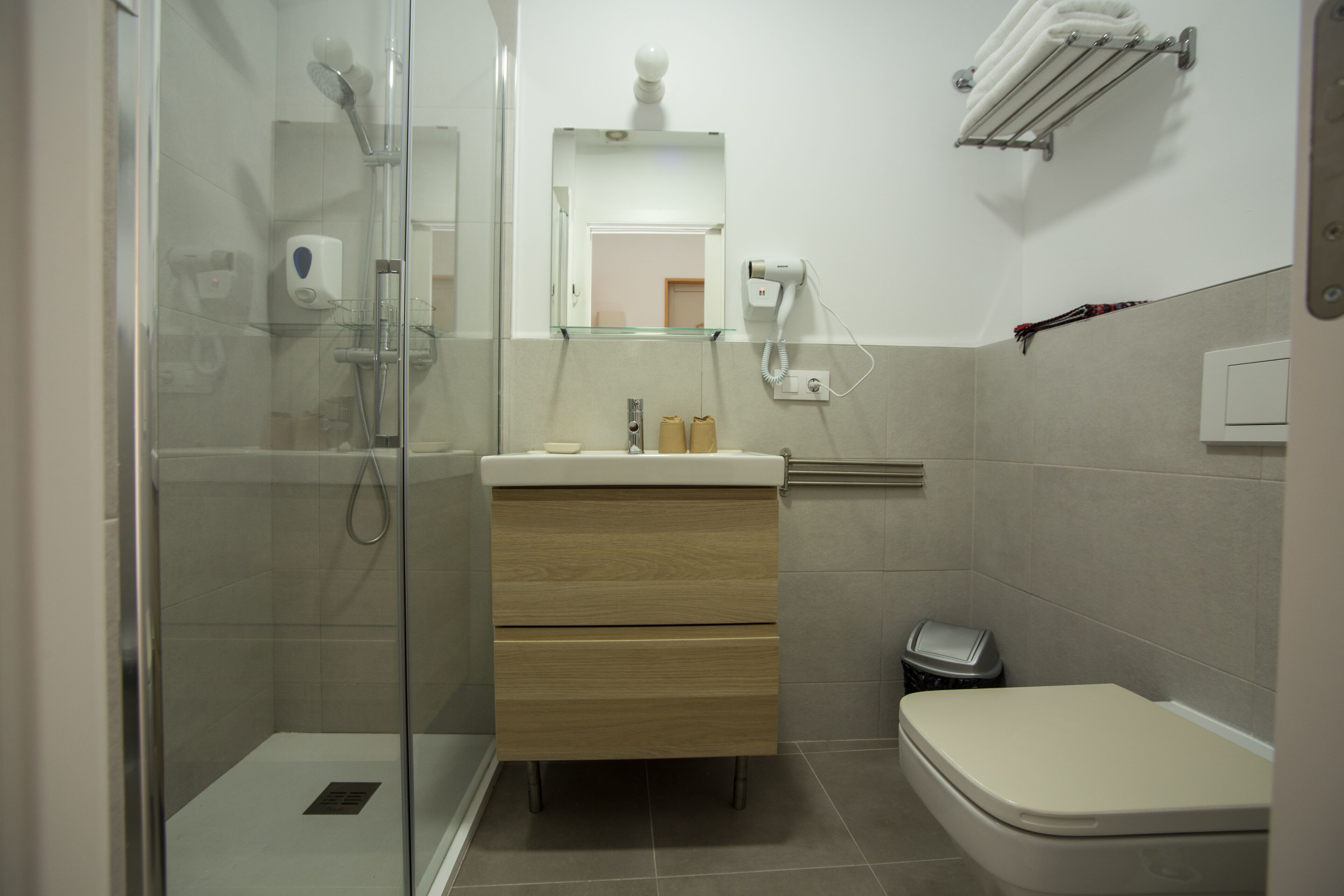 A modern bathroom with a glass-enclosed shower, a wooden vanity with a mirror, and a toilet.