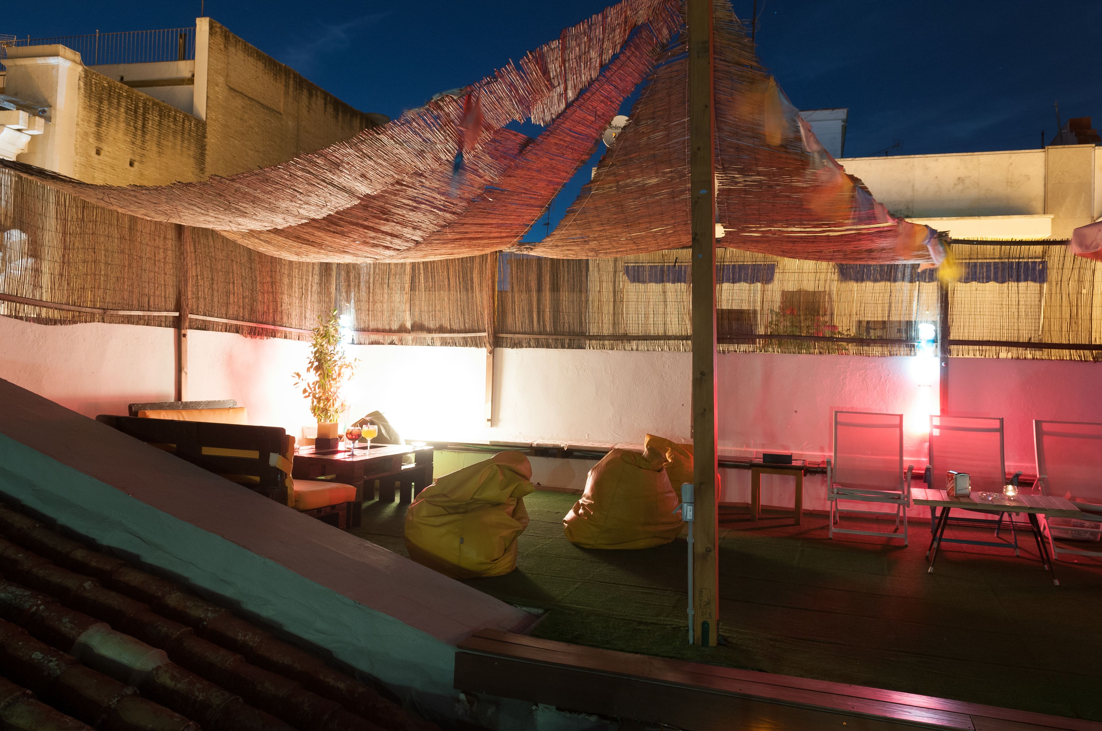 An outdoor seating area with a thatched roof, tables, chairs, and a potted plant.