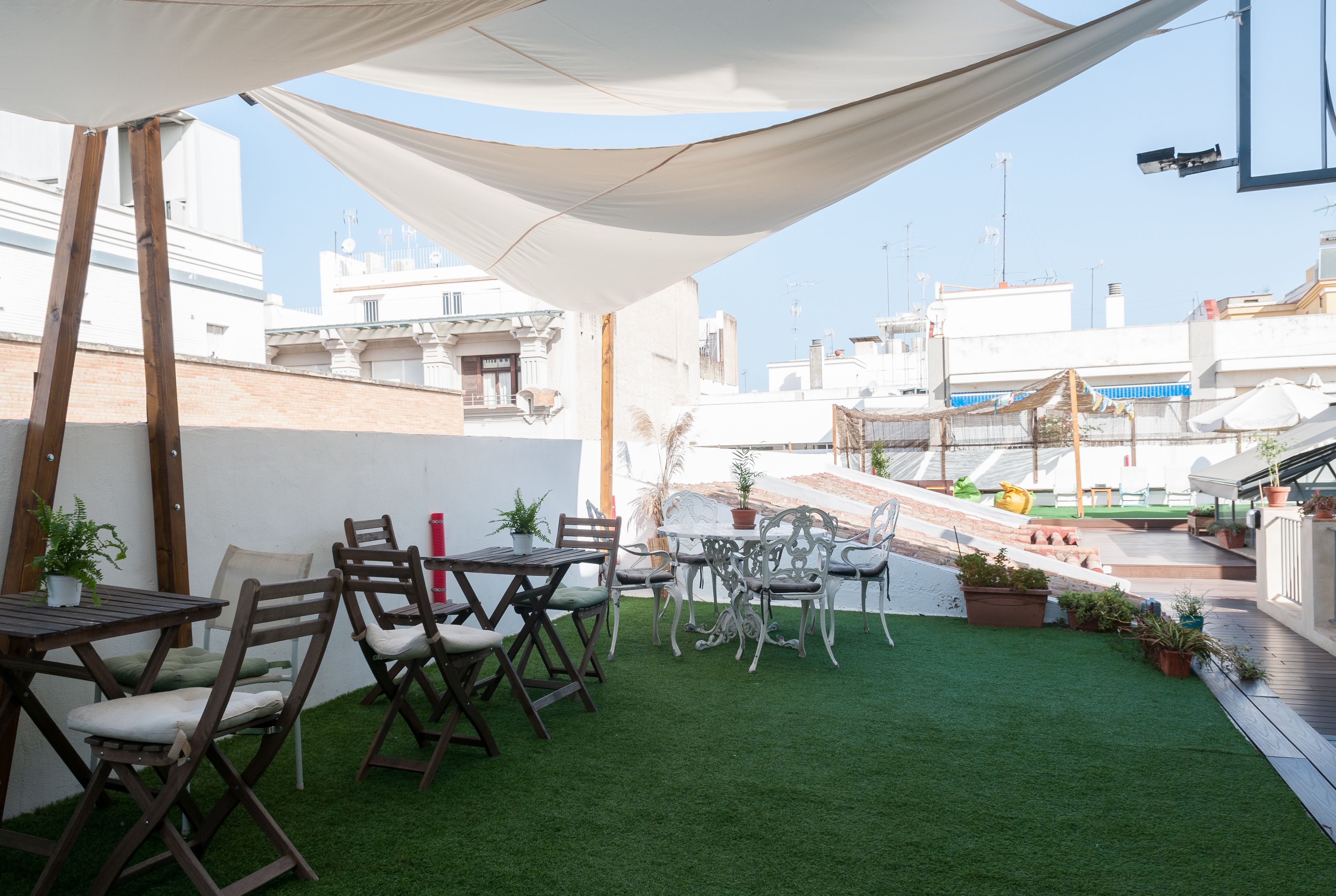 An outdoor patio with wooden tables and chairs, surrounded by potted plants and a white canopy.