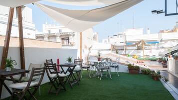 An outdoor patio with wooden tables and chairs, surrounded by potted plants and a white canopy.
