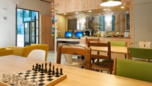 A modern office space with wooden panel walls, a central table with chess, and multiple computer monitors. - The Nomad Hostel (Seville)