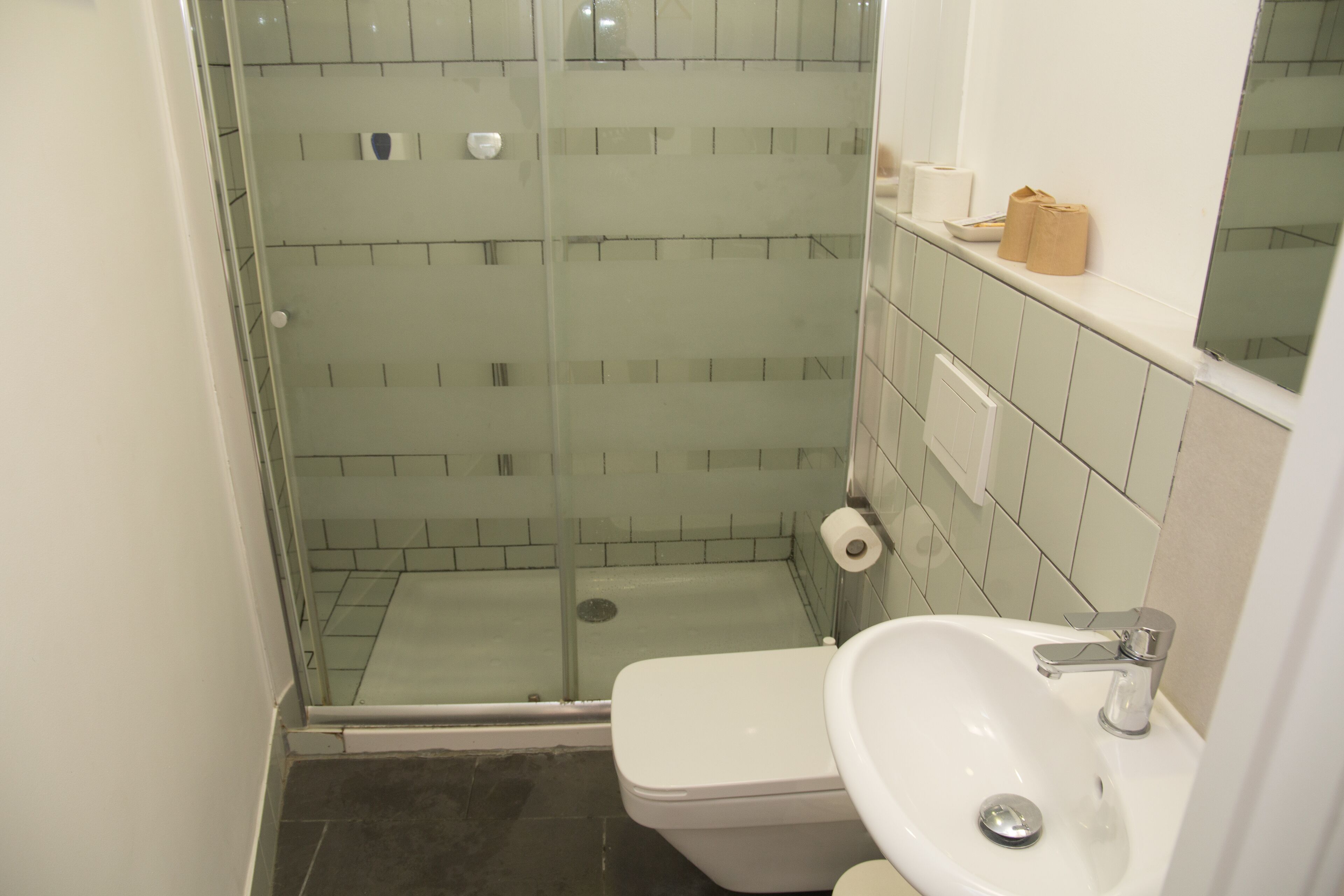 A bathroom with a glass shower enclosure, a white toilet, and a sink with a mirror above it.