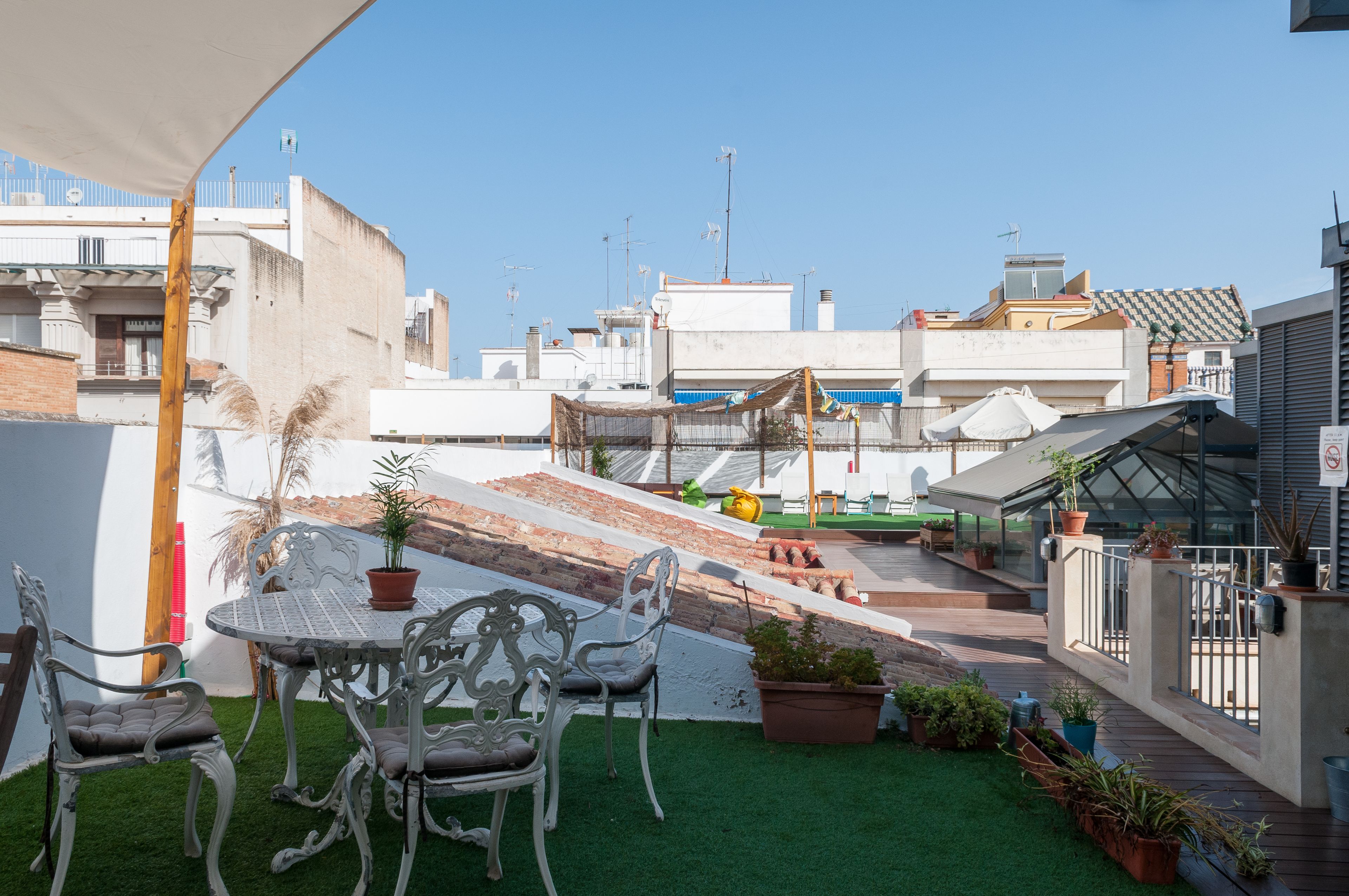A rooftop terrace with a table and chairs, potted plants, and a view of the cityscape.