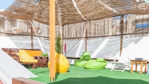 A covered outdoor area with a slide, green artificial turf, and colorful flowers. - The Nomad Hostel (Seville)