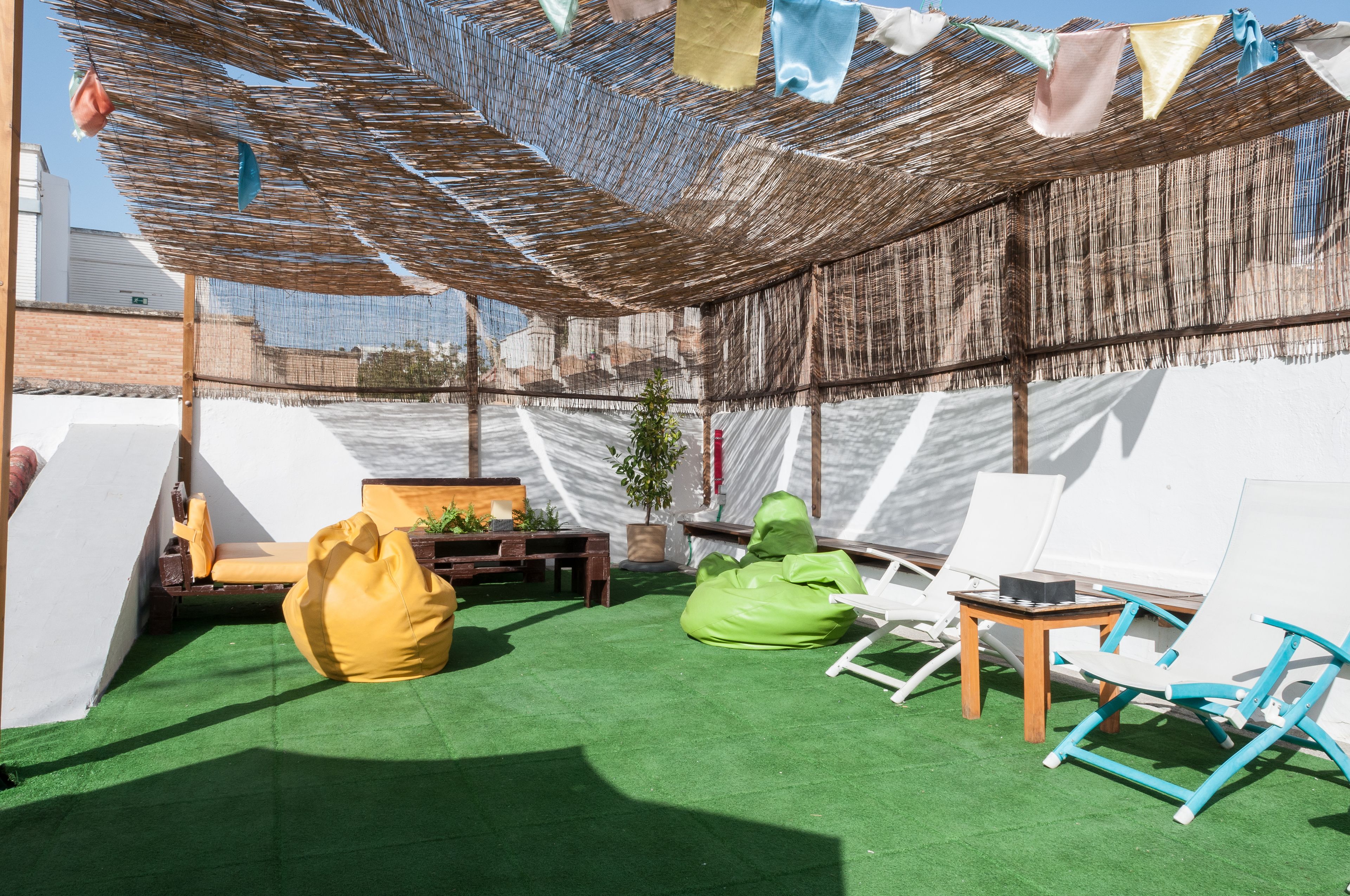 An outdoor seating area with green artificial turf, white and blue lounge chairs, a yellow bean bag, and a small wooden table.