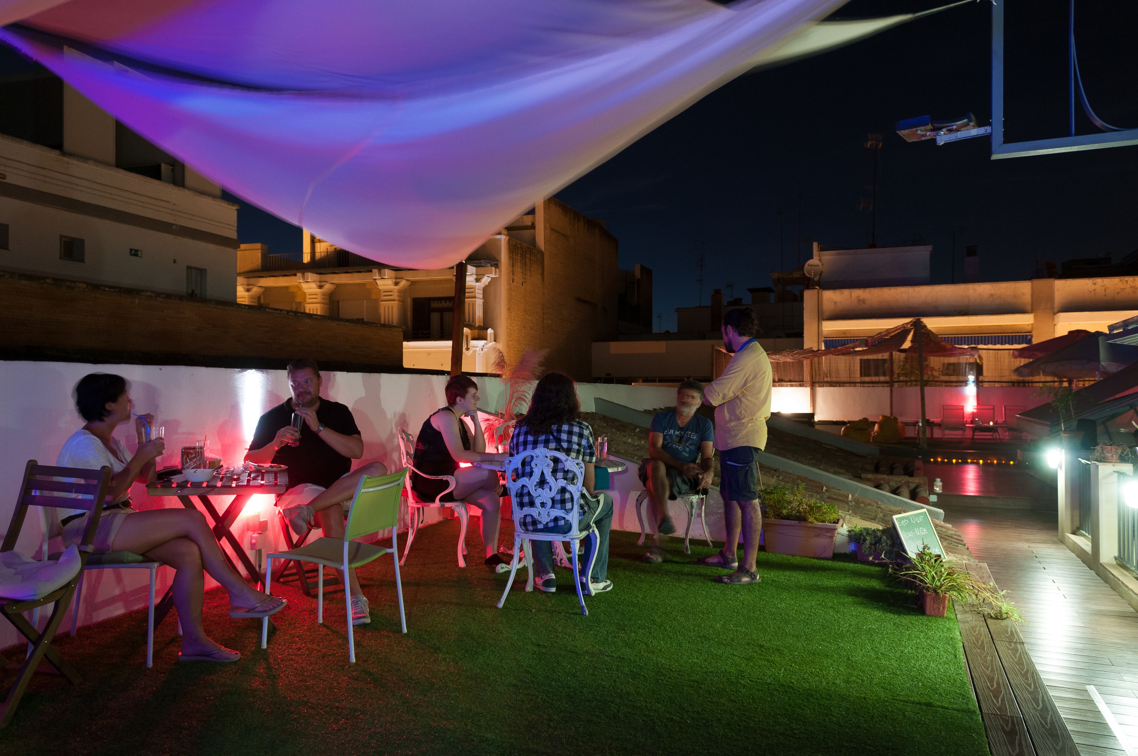 Een terras met tafels en stoelen, omringd door een lage muur en gazon.