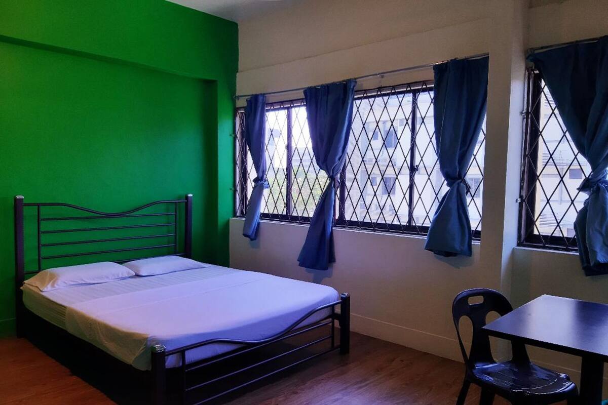 A room with a bed, a table, and two windows with curtains.