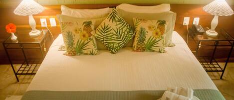 A neatly made bed with floral pillows, two bedside tables with lamps, and a green quilted bedspread.