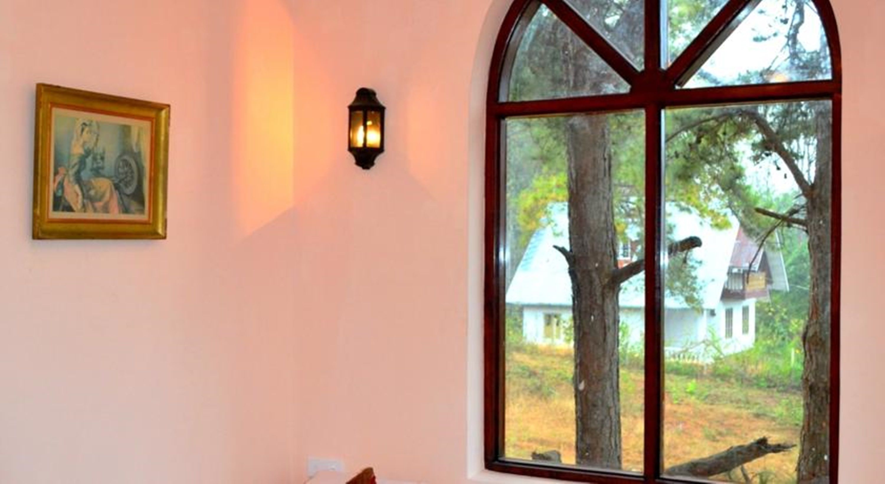 Una habitación con un gran ventanal arqueado, una lámpara fijada a la pared y un cuadro enmarcado.