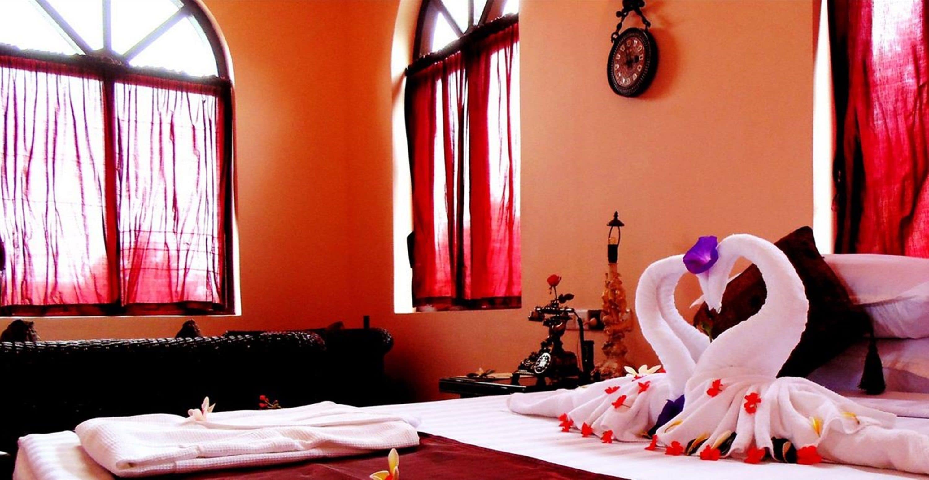A hotel room with a bed, a black sofa, a wall clock, and a decorative item resembling a swan.