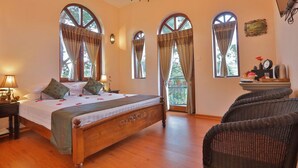 Une chambre à coucher avec un lit en bois, de grandes fenêtres en arc de cercle, un lustre et des fauteuils en osier.
