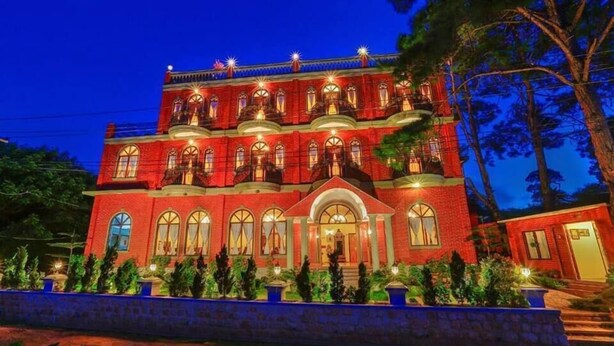 Un grand immeuble à plusieurs étages, doté d’une façade rouge et de nombreux balcons, entouré d’arbres.