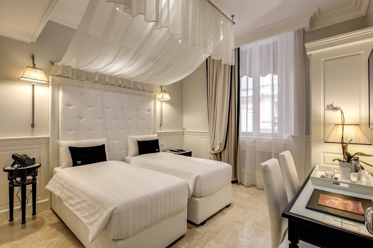 A hotel room with two beds, a desk with a lamp, a telephone, and a chair.