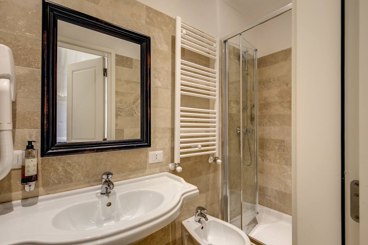 A bathroom with a large mirror, two sinks, a glass shower enclosure, and a towel rack.