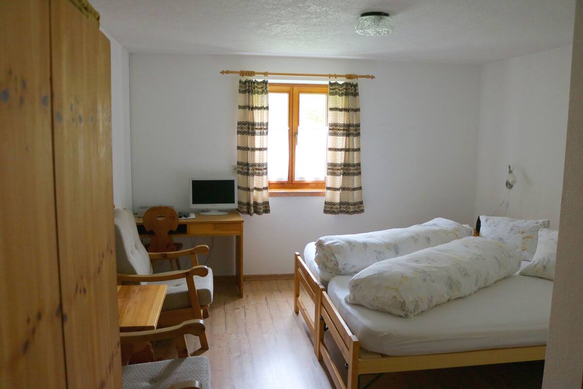 A bedroom with a wooden bed, a desk with a computer, and a chair.