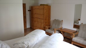 Una habitación con dos camas, un armario de madera, una silla, una mesita y un espejo en la pared.