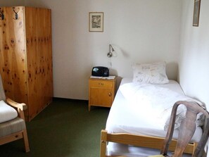 Una habitación con una cama de madera, una mesita de noche de madera con un radio, un armario de madera y una silla.