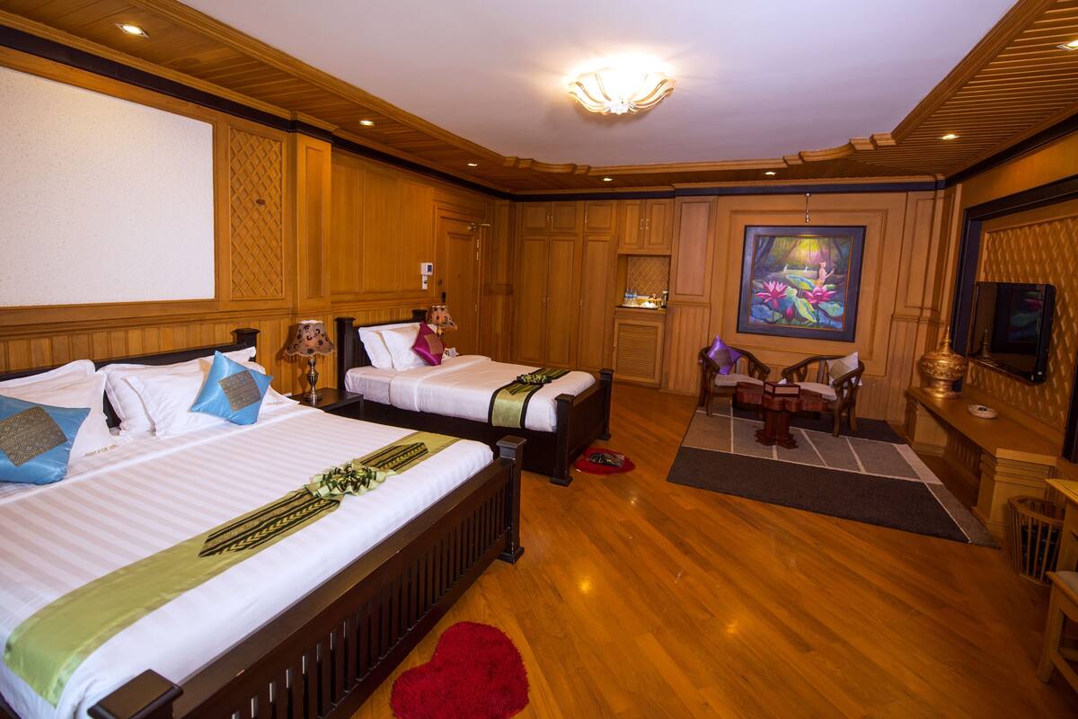 A hotel room with two beds, wooden paneling, a painting, and a television.