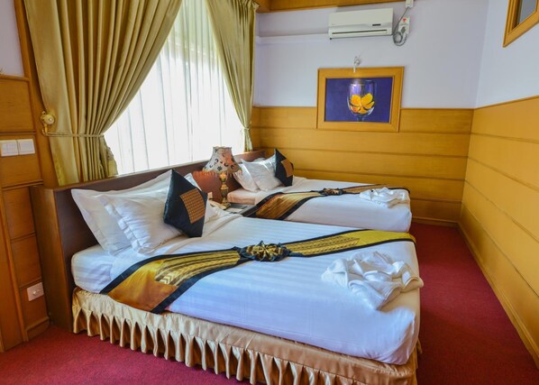 Habitación de hotel con dos camas, alfombra roja, ventana con cortinas, equipo de aire acondicionado y un cuadro en la pared.