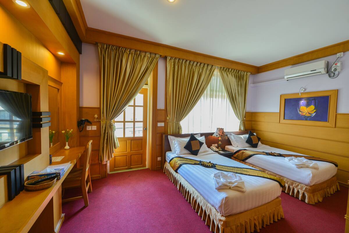 A hotel room with two beds, a desk, a television, and a large window with curtains.