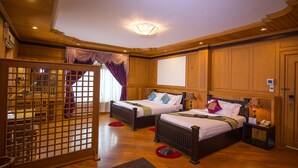 A hotel room with two beds, wooden paneling, a large window, and a traditional-style ceiling light. - Shwe Kyun Hotel (Taunggyi)