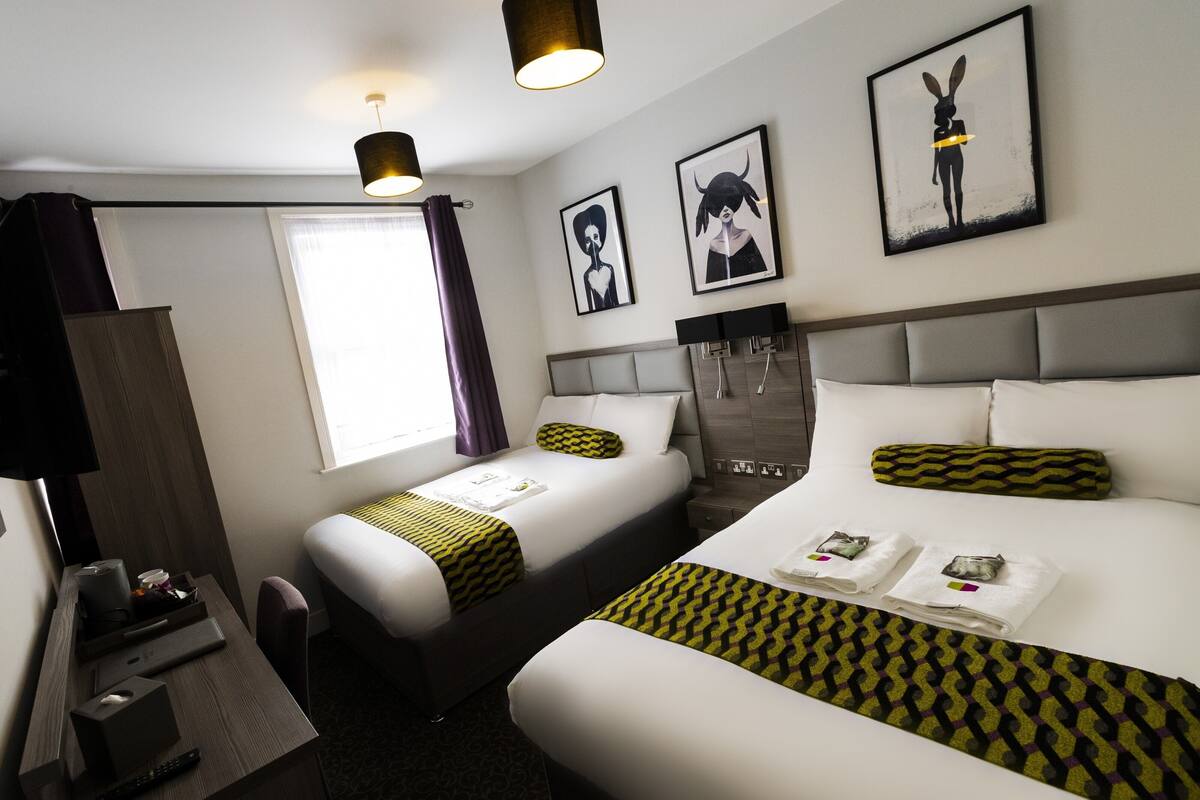 A hotel room with two beds, a desk, a TV, and artwork on the walls.
