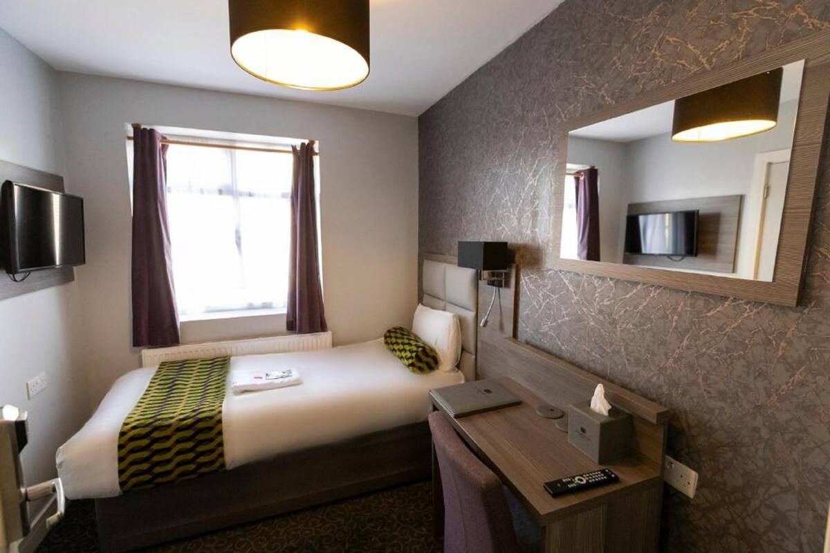 A hotel room with a bed, a desk with a computer, a TV, and a mirror.