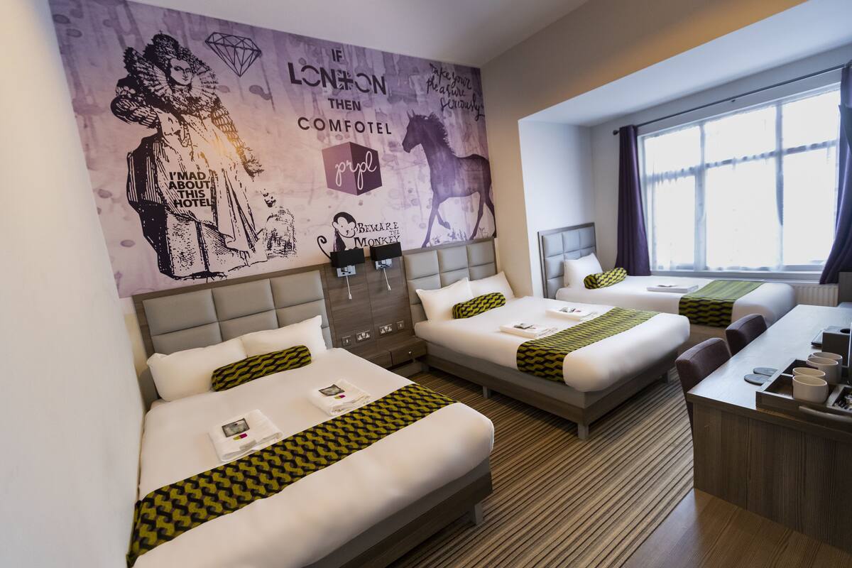 A hotel room with two beds, a desk, and a large window.