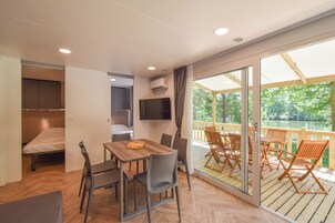Una habitación moderna con una mesa y sillas de madera, una cama, un televisor y un balcón con vista a un lago.