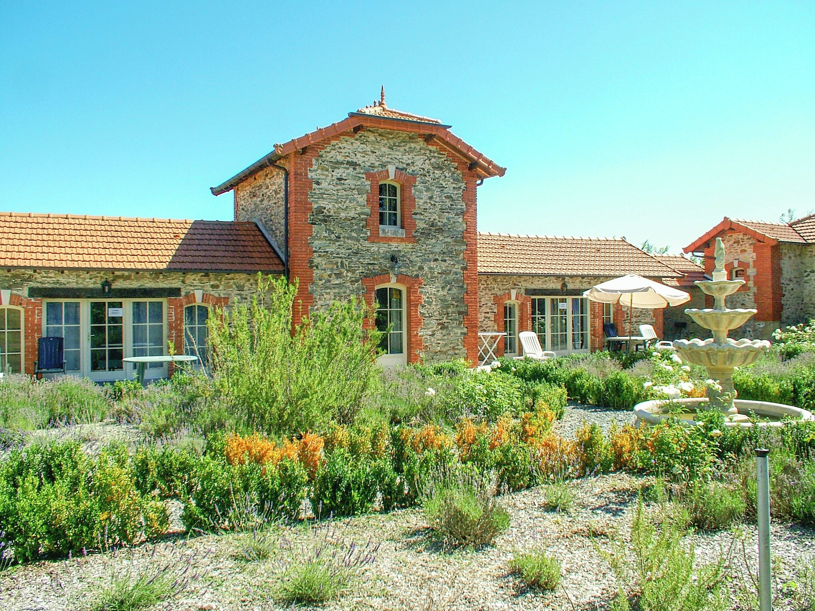 A stone building with a tiled roof, a fountain, and outdoor seating.