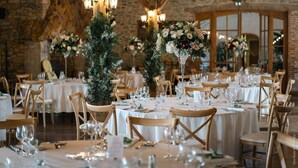 Ein Festsaal mit runden Tischen, Holzhöhlen und floralen Mittelstücken.