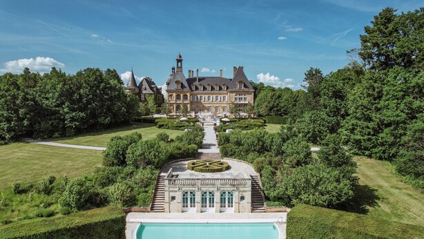 Ein großes, historisches Herrenhaus mit einem formellen Garten, einem zentralen Pool und einer symmetrischen Anordnung.