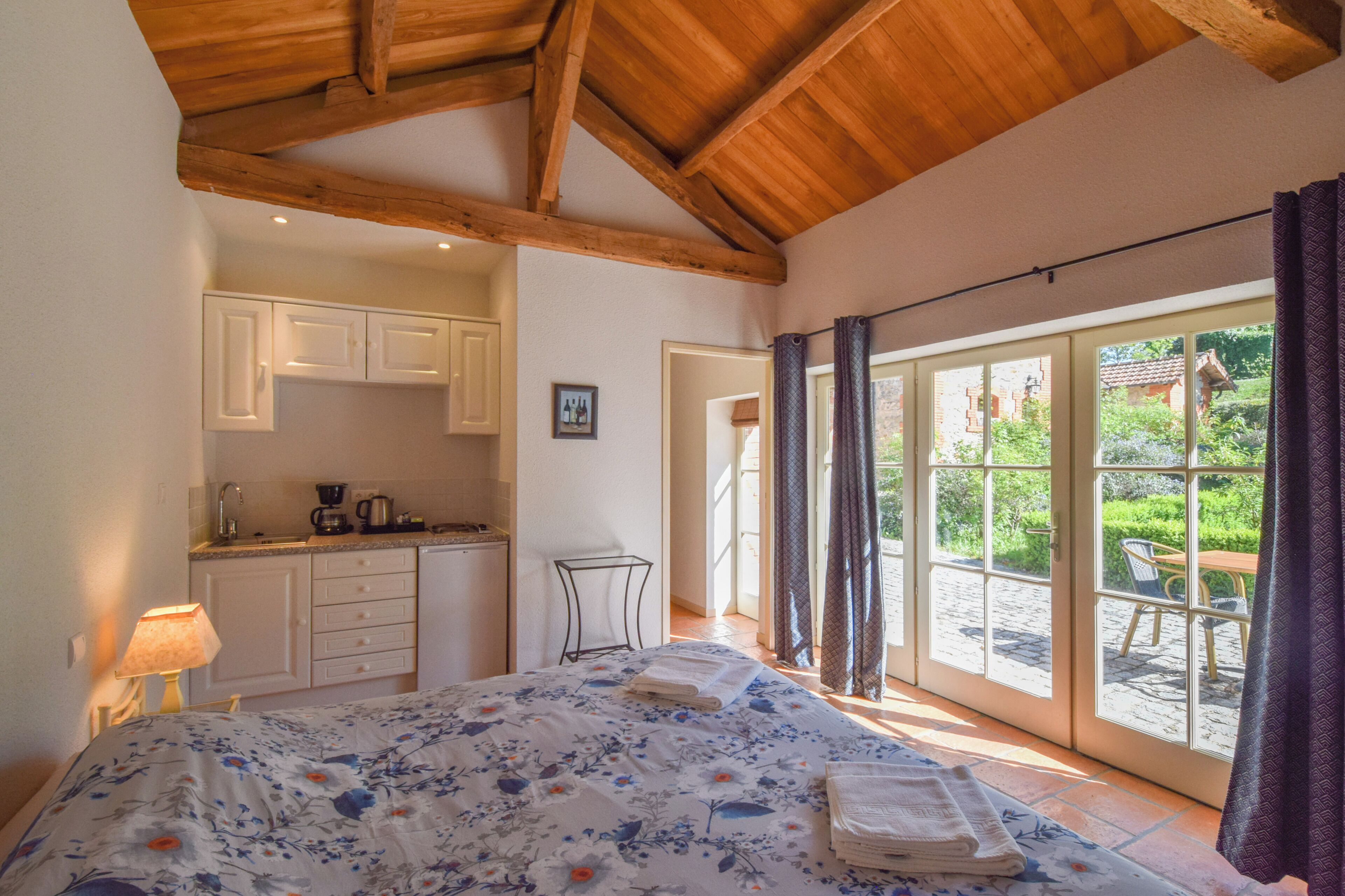 Une chambre à coucher avec un lit, une table de chevet, une fenêtre avec des rideaux et une vue sur un jardin.