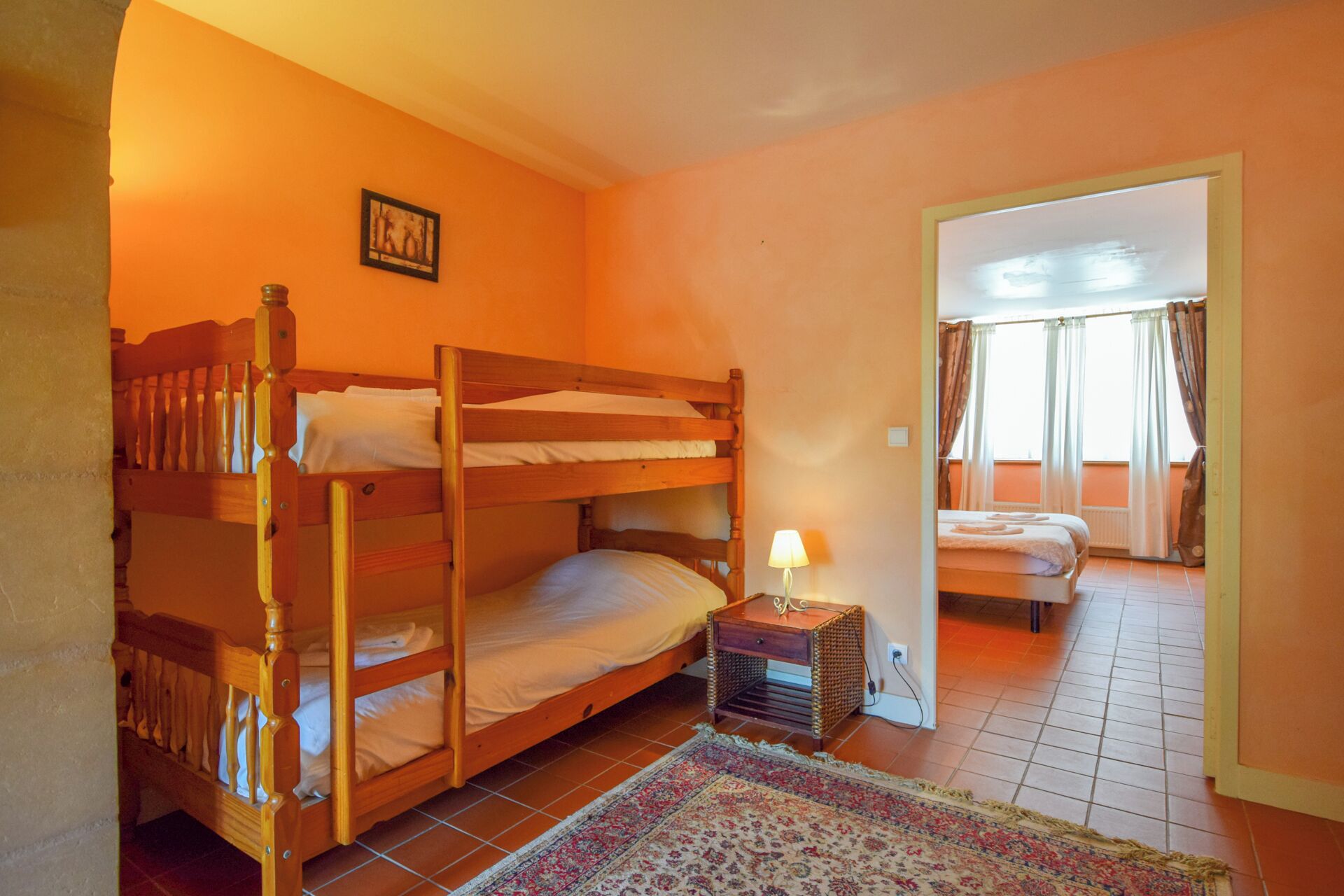 Ein Schlafsaalzimmer mit Etagenbetten, einem kleinen Nachttisch mit Lampe und einem gemusterten Teppichboden.