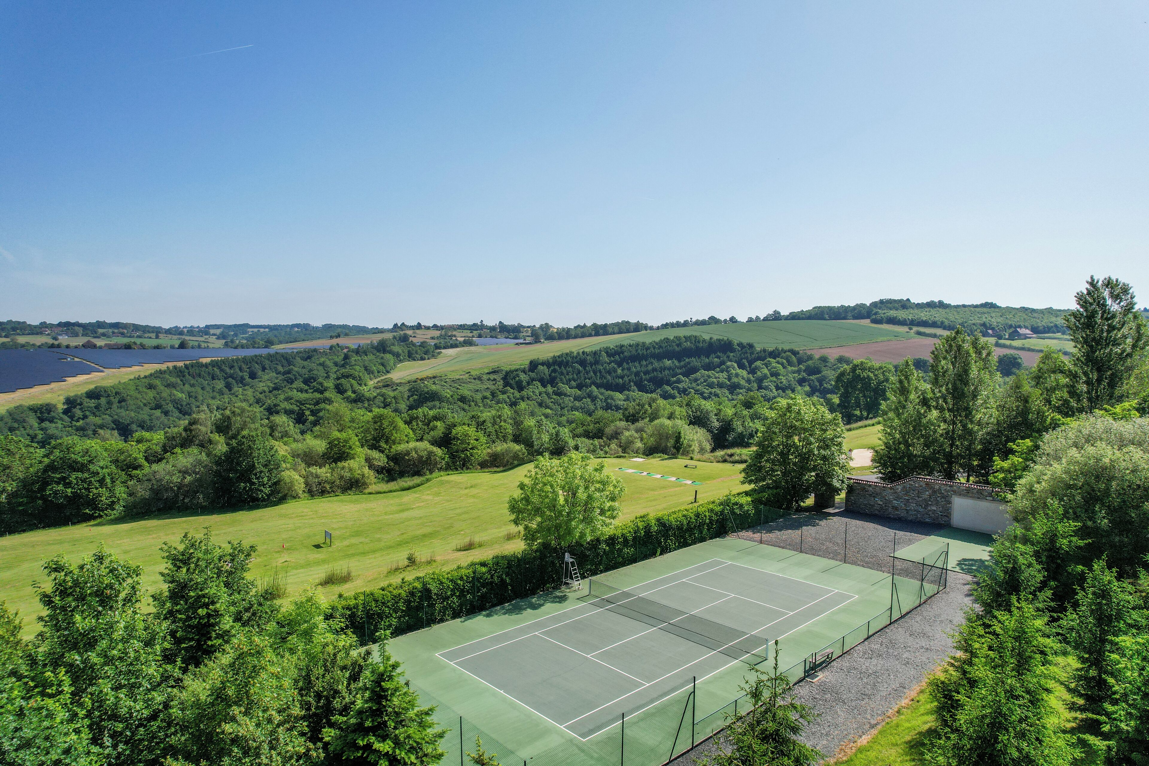 A tennis court surrounded by lush greenery and a lake in the background.