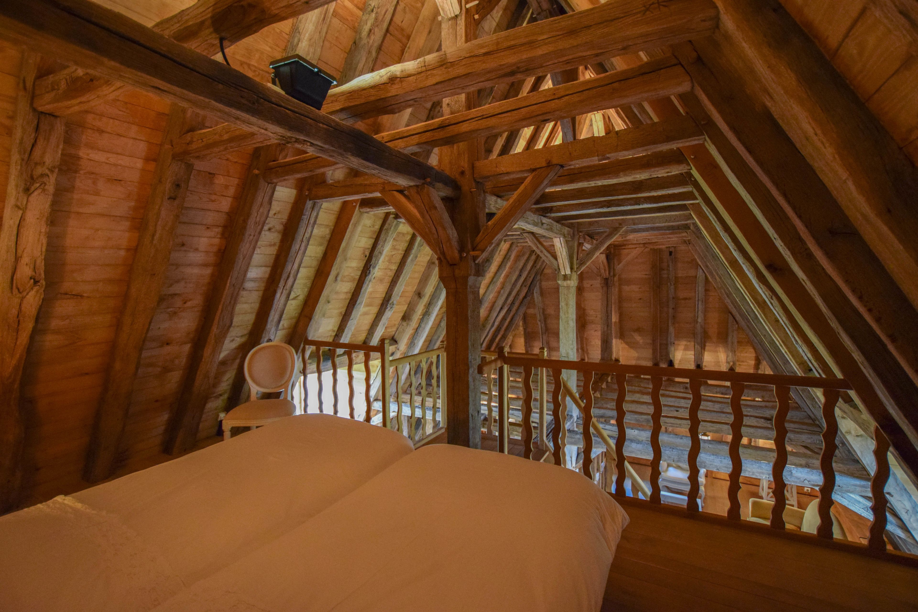 A wooden attic bedroom with a sloped ceiling, a bed, and a chair.