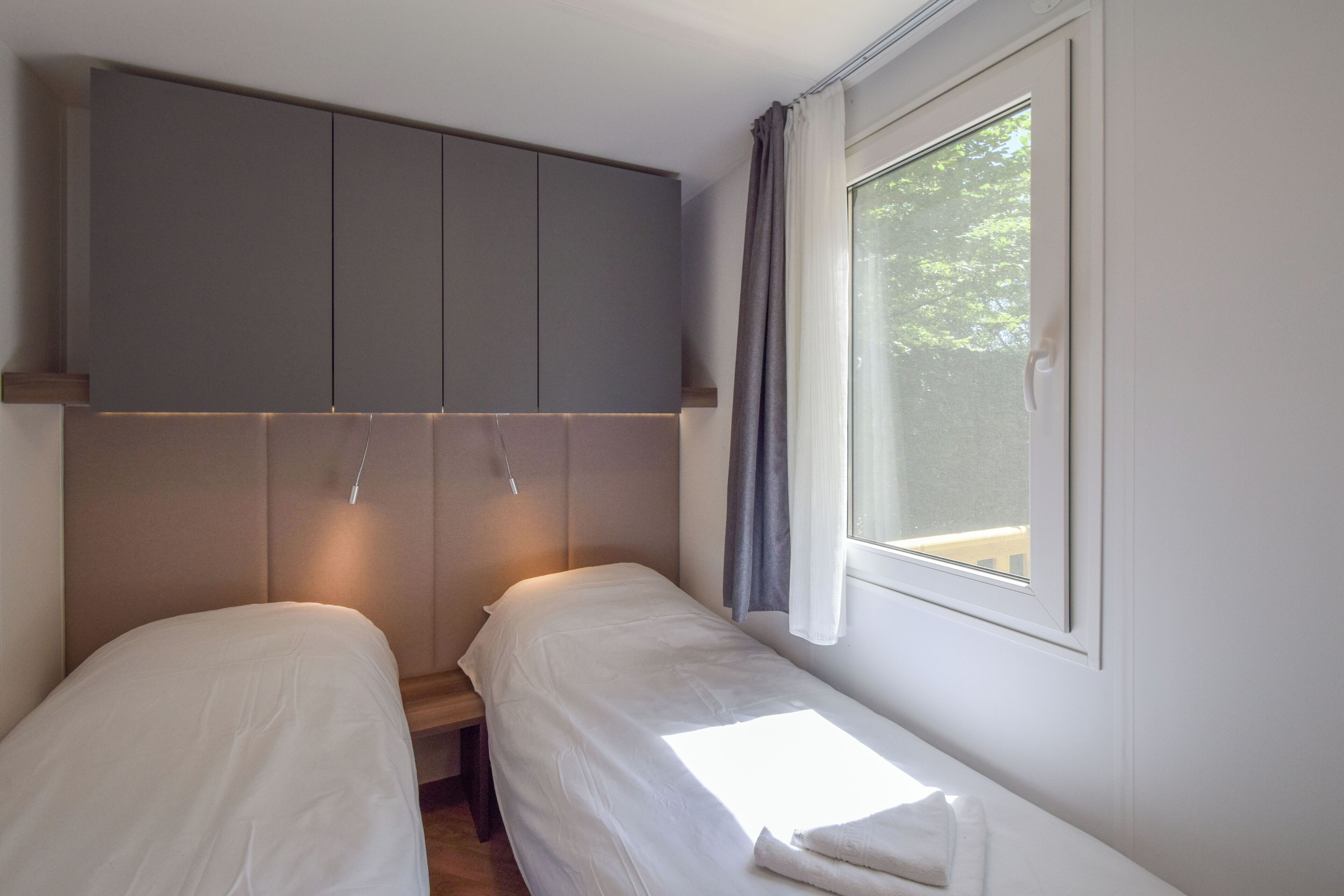 Een slaapkamer met twee eenpersoonsbedden, een kledingkast en een raam met gordijnen.