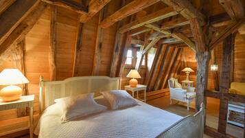 Een gezellig slaapkamer op zolder met een bed, twee nachtkastjes met lampen, een stoel en een kleine tafel.