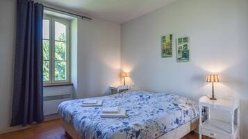 Un dormitorio con una cama, dos mesitas de noche, un ventanal con cortinas y dos lámparas de pared.