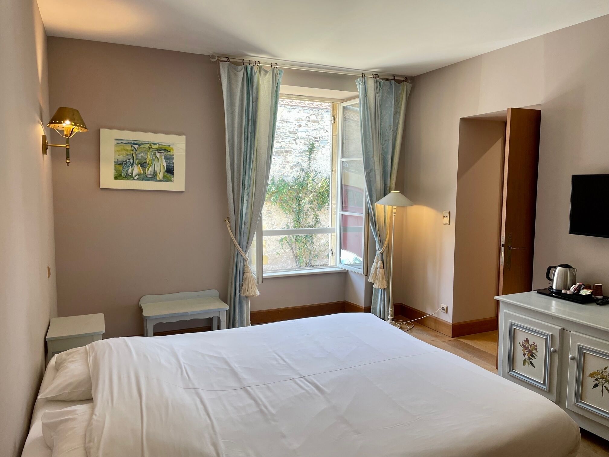 Una habitación de hotel con una cama, un escritorio, una lámpara, televisión y una ventana con cortinas.