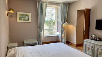 Una habitación de hotel con una cama, un escritorio, una lámpara, televisión y una ventana con cortinas.