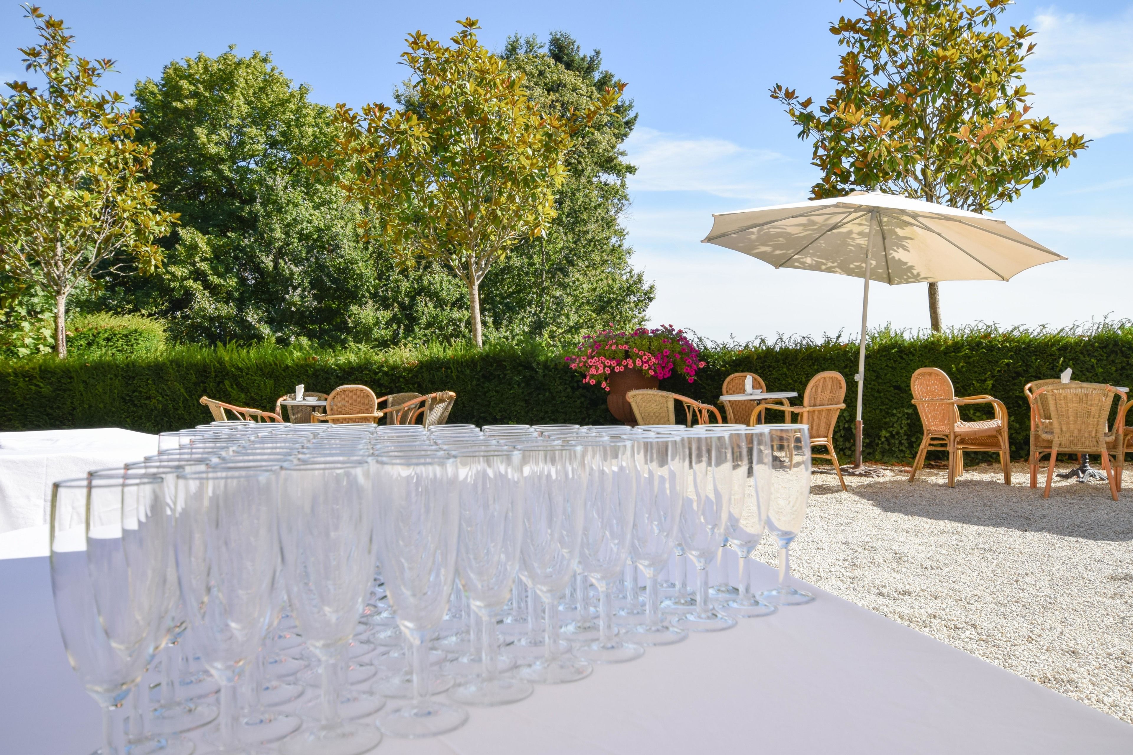 Een tafel gedekt met verschillende wijnglazen, buitenstoelen en een grote parasol.