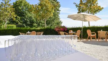 Ein Tisch ist gedeckt mit mehreren Weingläsern, Gartenstühlen und einem großen Sonnenschirm.