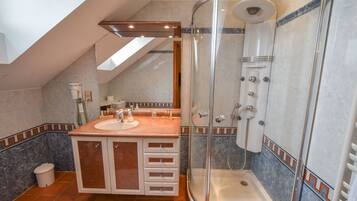 Un baño moderno con ducha envuelta en vidrio, tocador con lavamanos y piso de baldosas.