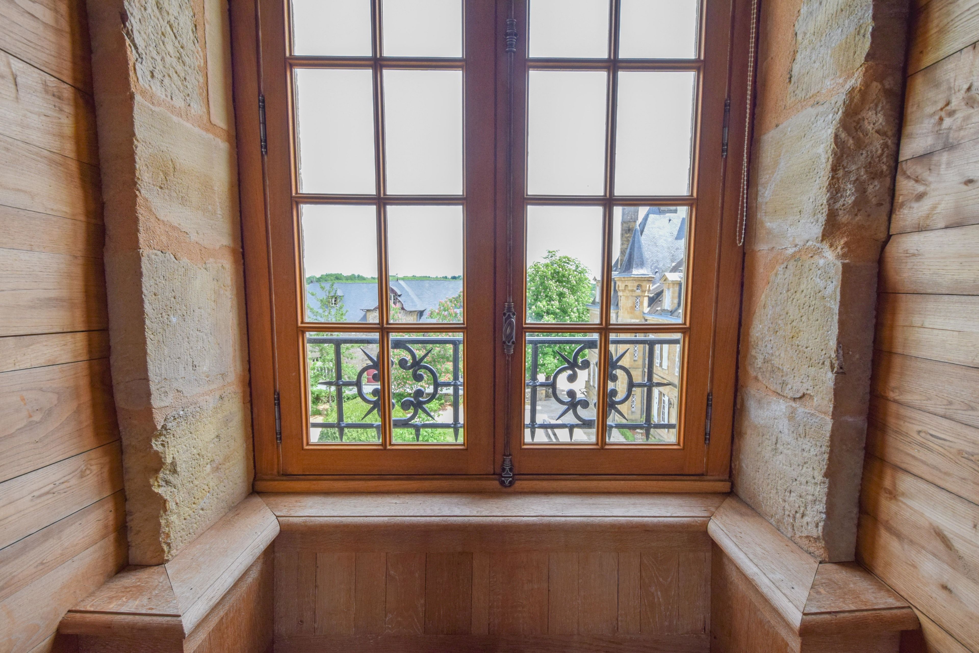 Une fenêtre à cadre en bois donnant sur un balcon et sur les bâtiments environnants.