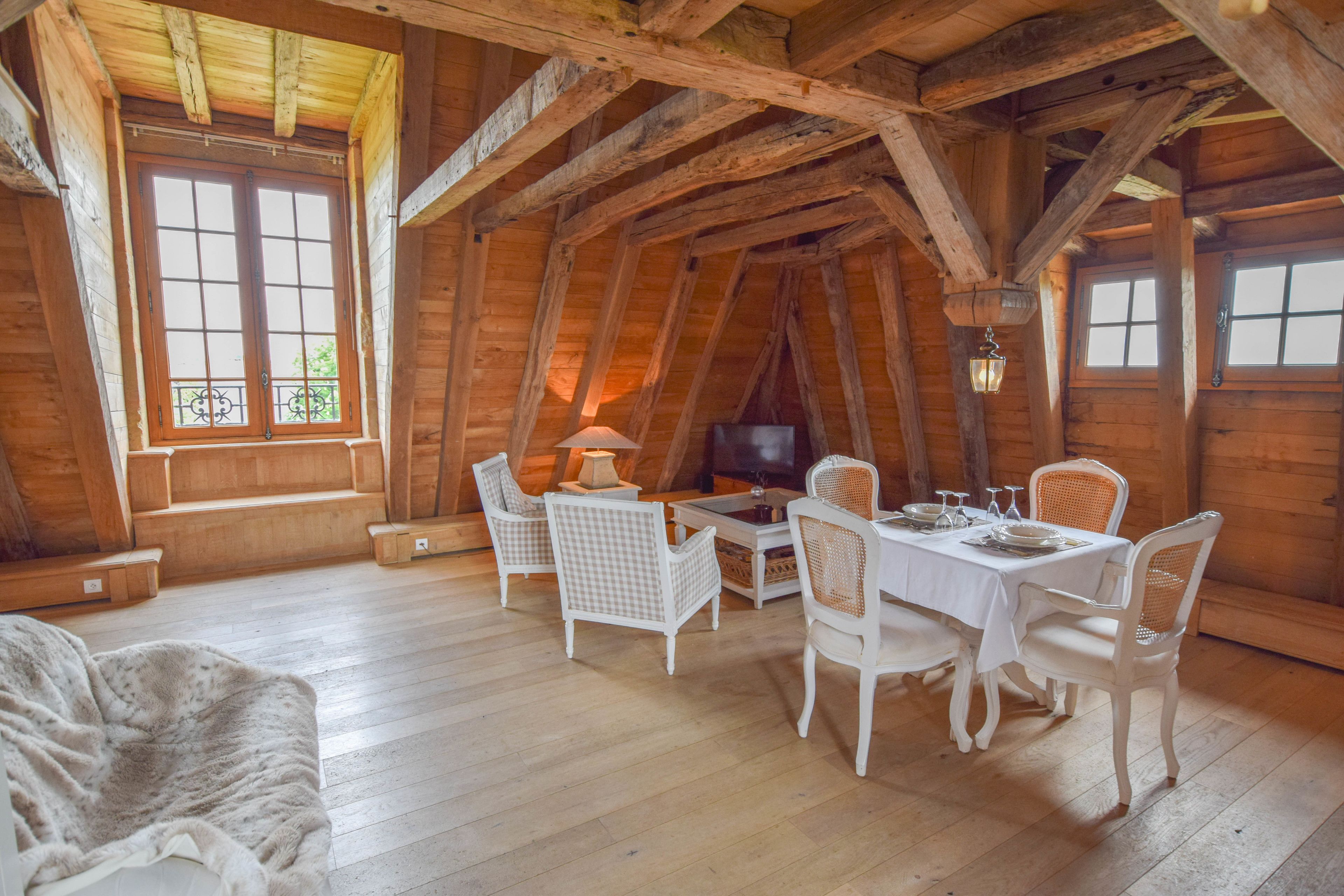 Une chaleureuse cabane en bois dotée d’un coin repas avec des chaises en osier blanc et une table dressée pour quatre personnes.