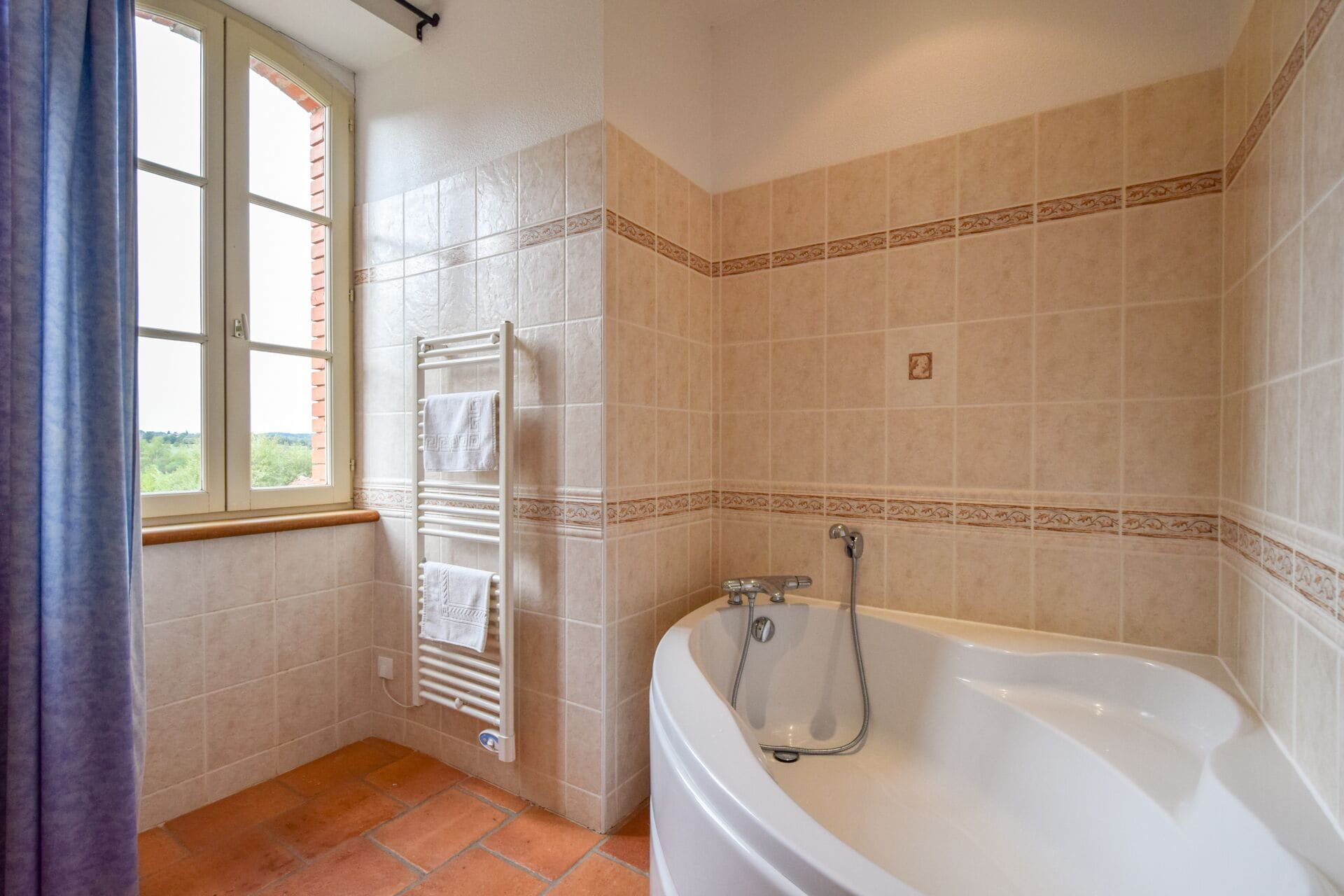 Une salle de bain avec une baignoire, un porte-serviettes et une fenêtre avec des rideaux.